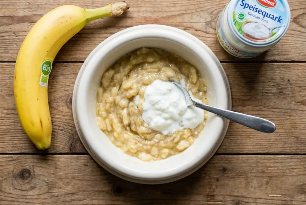 Hundenapf mit zerdrückter Banane und etwas Quark. Daneben liegt eine frische Banane.